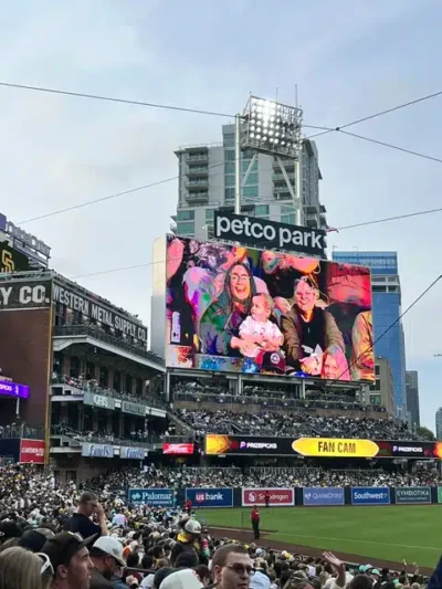 Petco Park’s giant video board showing a family photo during a baseball game with fans in the stands surrounding the field.