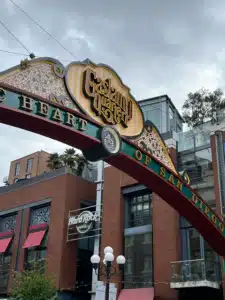 Decorative street arch in the Gaslamp Quarter reading 'Heart of San Diego' with brick buildings and a Hard Rock Hotel sign in the background under a cloudy sky.