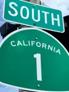 Southbound California State Route 1 sign mounted under a large green 'SOUTH' sign against a blue sky.
