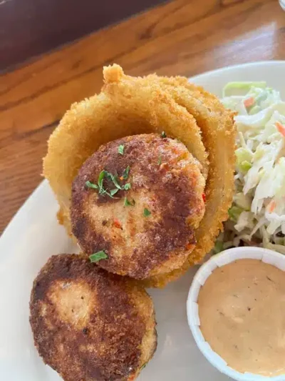 Crispy fried onion rings with a breaded croquette resting on top, served with coleslaw and a creamy dipping sauce on the side.