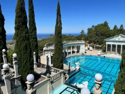 Terrace with a bright blue tiled pool, classical statues, and tall cypress trees overlooking the sea.