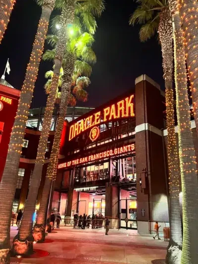 Oracle Park entrance at night, palm trees wrapped in lights flame the walkway toward the stadium signage, Giants home venue.