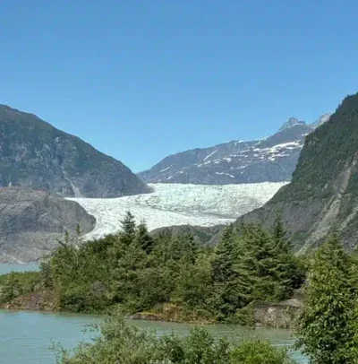 Mendenhall Glacier - TruFlex Media Glacier between mountains above a turquoise lake; foreground shows trees and a small sign on a sandy shore.