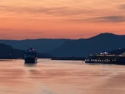 Leaving Port - TruFlex Media Sunset over a wide river with two lit cruise ships near the shore and distant hills in the background.