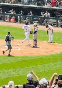 Well Done - TruFlex Media Baseball scene at home plate: runner in white (No. 5) advances toward home while catcher and an umpire stand nearby, with a batter looking on and fans in the stands.